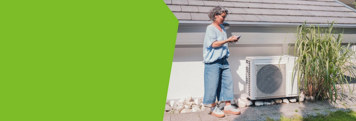 Person steht mit einem Smartphone vor einer Wärmepumpe im Freien.